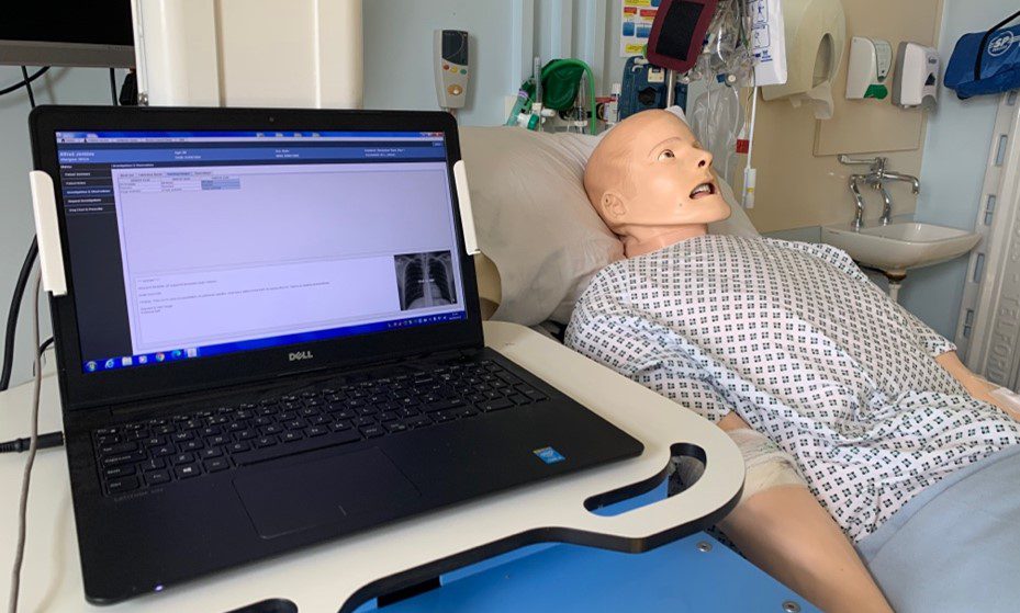 Male dummy laying on hospital bed with laptop and monitoring equipment next to him